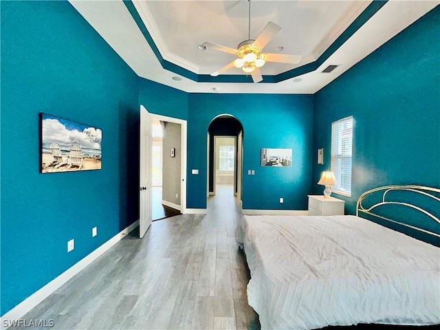 unfurnished bedroom featuring baseboards, visible vents, arched walkways, a raised ceiling, and wood finished floors