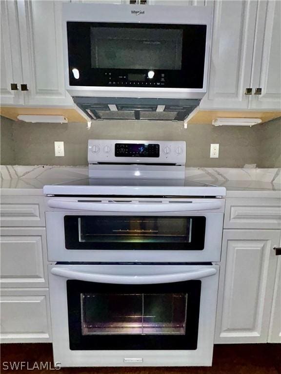 interior details with tasteful backsplash, double oven range, stainless steel microwave, and white cabinetry