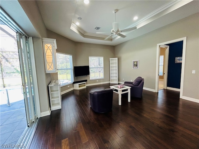 living room featuring dark wood-type flooring, crown molding, a tray ceiling, and ceiling fan