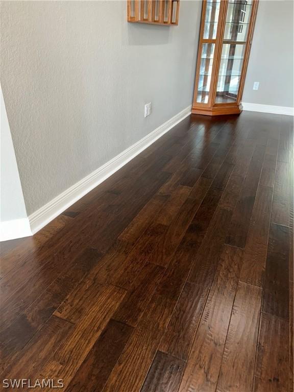 spare room featuring baseboards and dark wood-style flooring