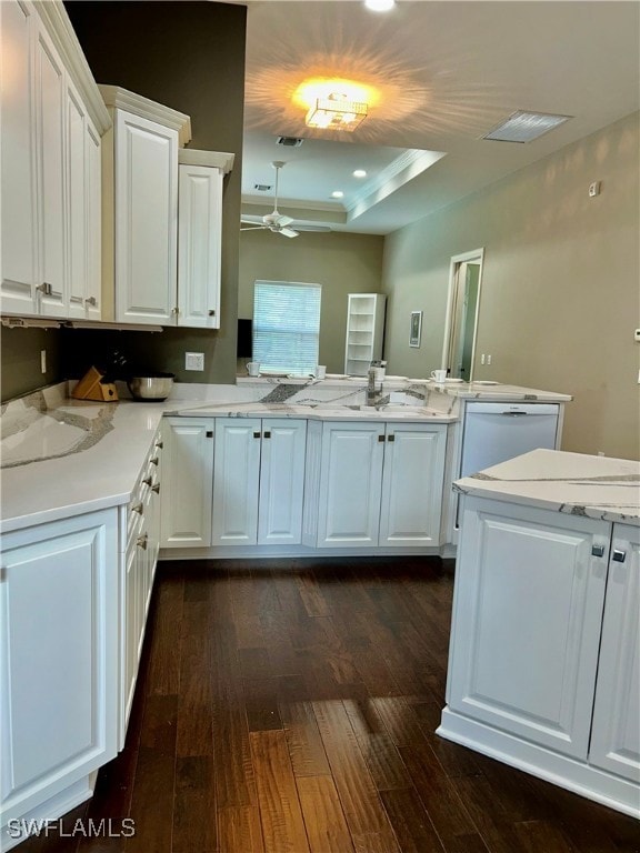 kitchen featuring white cabinetry, dark hardwood / wood-style flooring, kitchen peninsula, white dishwasher, and a tray ceiling