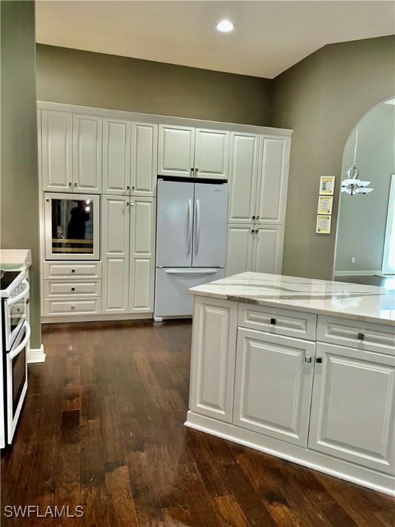 kitchen with dark wood-style floors, arched walkways, freestanding refrigerator, white cabinetry, and double oven range