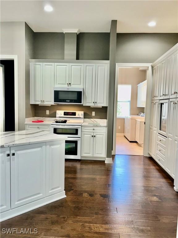 kitchen featuring washer and dryer, light stone counters, range with two ovens, and white cabinets