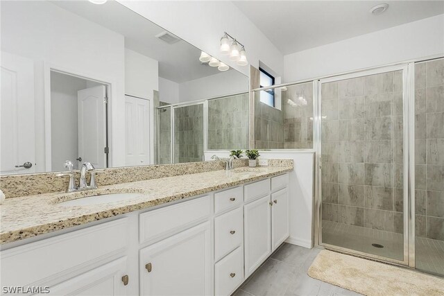 bathroom with a shower with shower door, vanity, and tile patterned floors