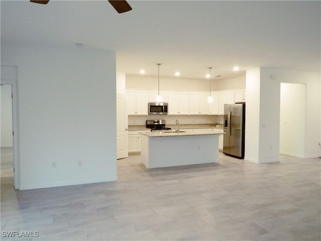 kitchen with appliances with stainless steel finishes, pendant lighting, white cabinets, and an island with sink