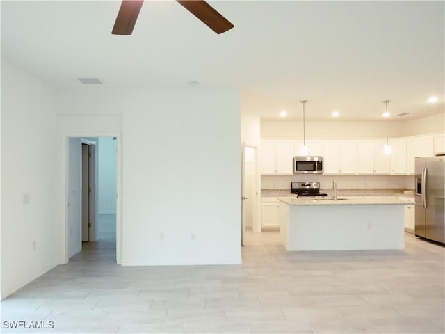 kitchen featuring appliances with stainless steel finishes, white cabinets, a center island with sink, and hanging light fixtures