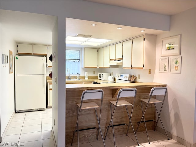 kitchen with kitchen peninsula, white appliances, sink, light tile floors, and a kitchen bar