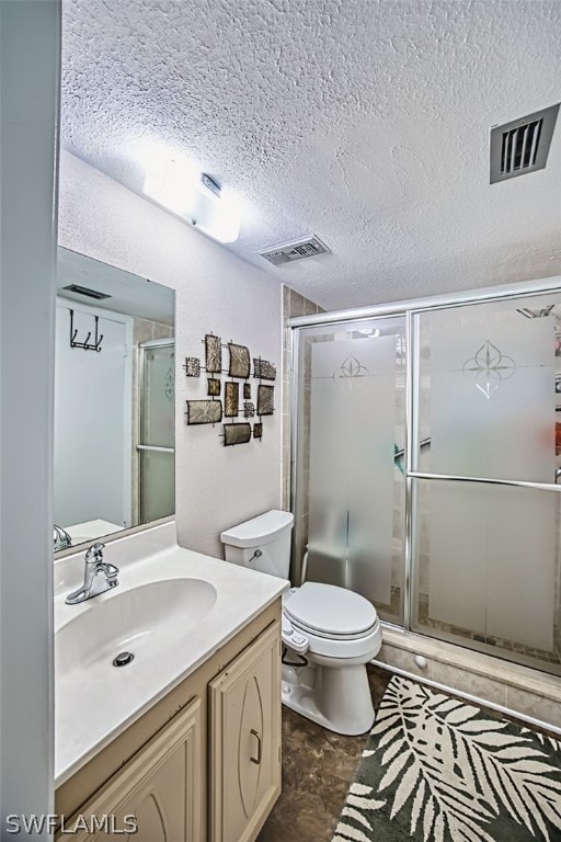 bathroom featuring vanity, toilet, a shower with door, and a textured ceiling