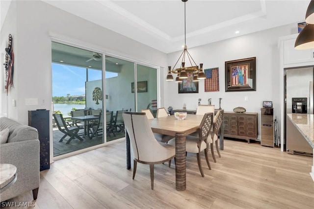 dining area with a water view, a tray ceiling, and light hardwood / wood-style floors