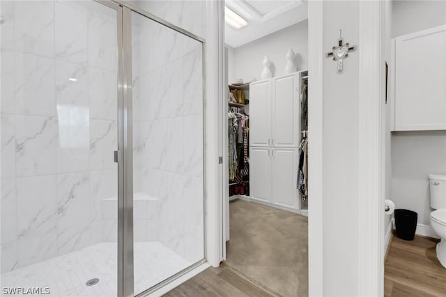 bathroom featuring a spacious closet, a stall shower, wood finished floors, and toilet