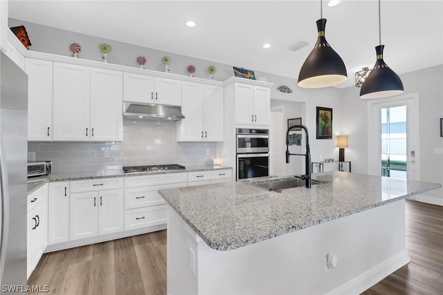 kitchen with sink, appliances with stainless steel finishes, hanging light fixtures, white cabinets, and a center island with sink