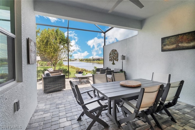 view of patio with a water view, ceiling fan, outdoor lounge area, and glass enclosure