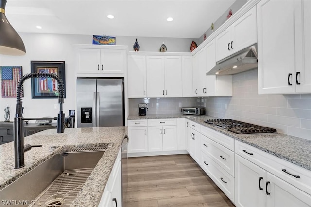 kitchen with white cabinets, appliances with stainless steel finishes, light wood-type flooring, under cabinet range hood, and a sink