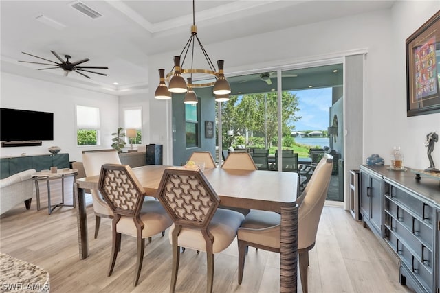 dining space with a raised ceiling, ceiling fan with notable chandelier, and light hardwood / wood-style flooring