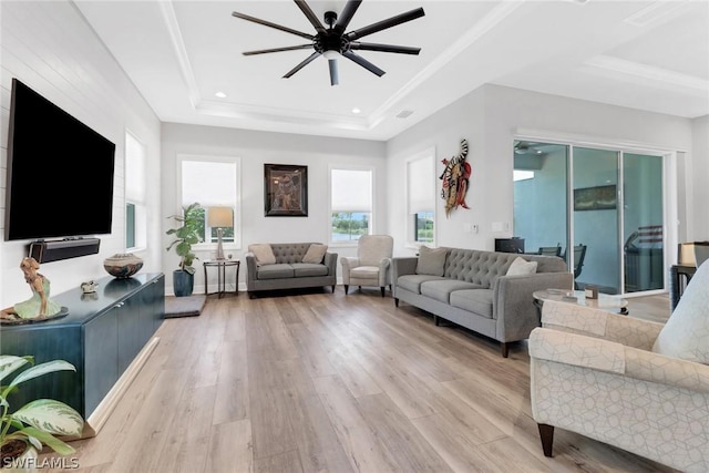 living room with a ceiling fan, a raised ceiling, crown molding, and light wood-style flooring