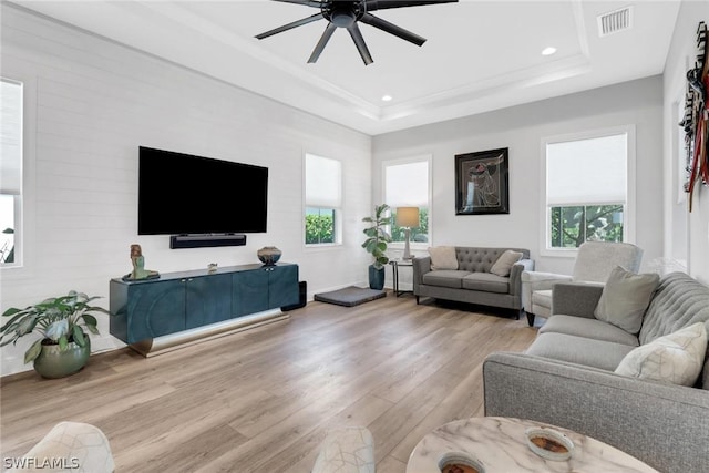 living room with a tray ceiling, recessed lighting, visible vents, ornamental molding, and wood finished floors