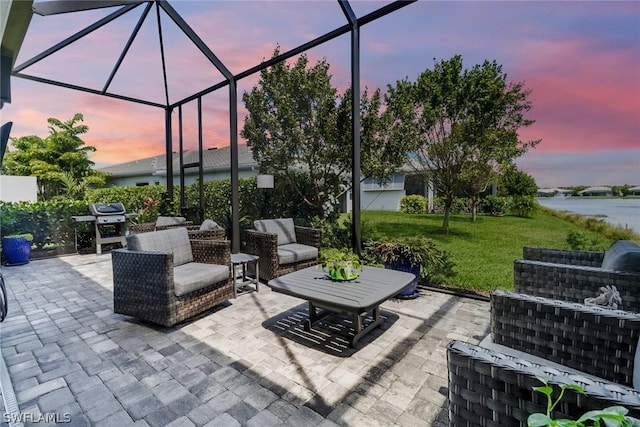 patio terrace at dusk featuring a lanai, a yard, an outdoor hangout area, grilling area, and a water view