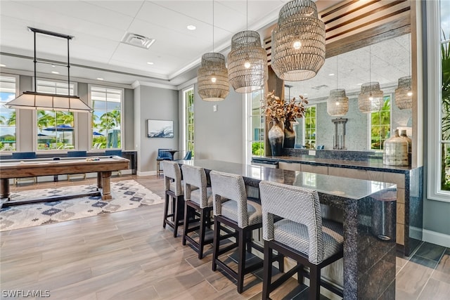 bar featuring crown molding, a healthy amount of sunlight, decorative light fixtures, and dark stone counters