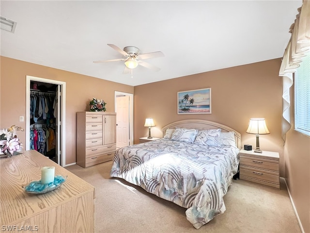 bedroom featuring light colored carpet, ceiling fan, a closet, and a walk in closet