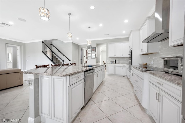 kitchen featuring white cabinetry, stainless steel appliances, an island with sink, wall chimney range hood, and pendant lighting