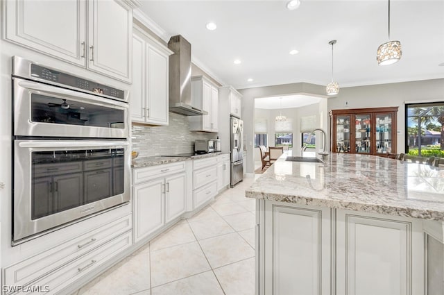 kitchen featuring double oven, decorative light fixtures, tasteful backsplash, wall chimney exhaust hood, and sink