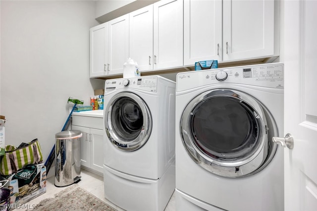 clothes washing area with light tile flooring, washer and dryer, and cabinets