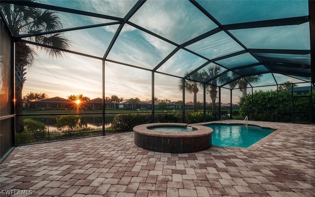 pool at dusk with an in ground hot tub, glass enclosure, and a patio area