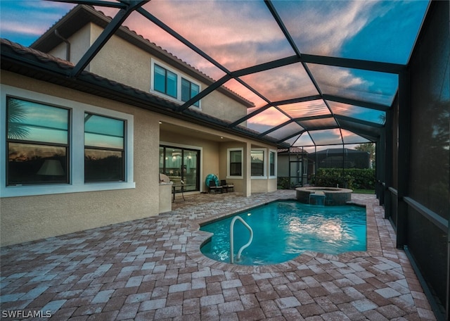 pool at dusk featuring a patio, an in ground hot tub, and glass enclosure