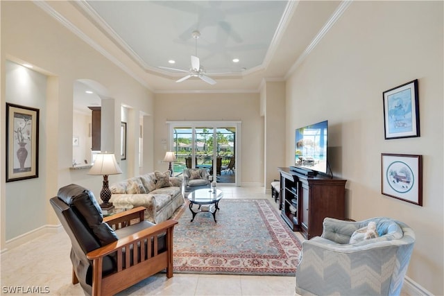living room featuring ceiling fan, a high ceiling, a tray ceiling, ornamental molding, and light tile patterned flooring
