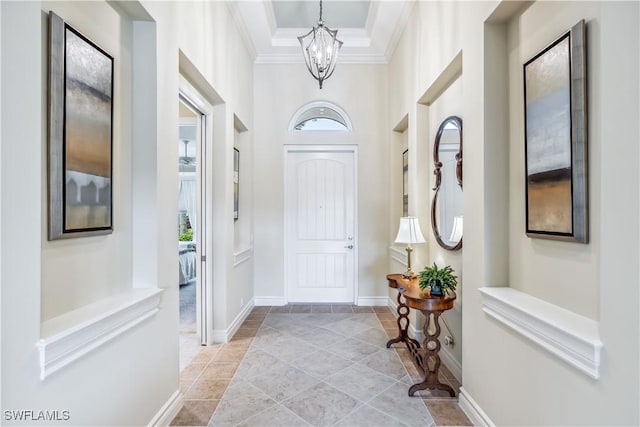 foyer with crown molding, a towering ceiling, light tile patterned flooring, a raised ceiling, and a chandelier