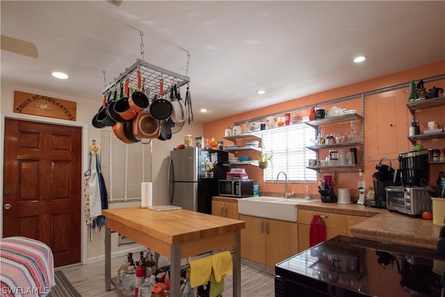 kitchen with sink, tile counters, light wood-type flooring, and stainless steel appliances