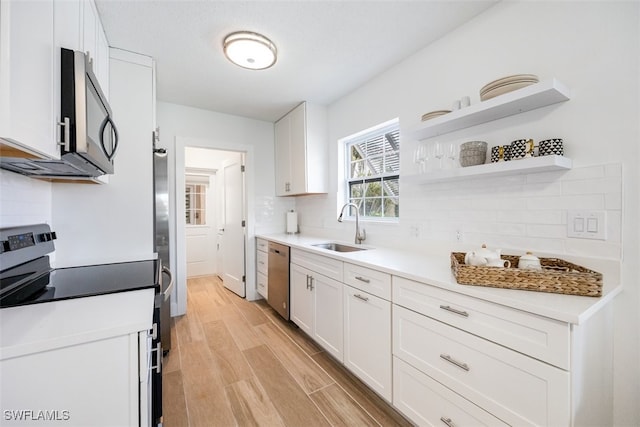 kitchen with white cabinets, sink, light hardwood / wood-style flooring, decorative backsplash, and appliances with stainless steel finishes