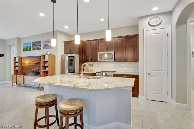 kitchen featuring light stone counters, a breakfast bar, a sink, stainless steel appliances, and backsplash