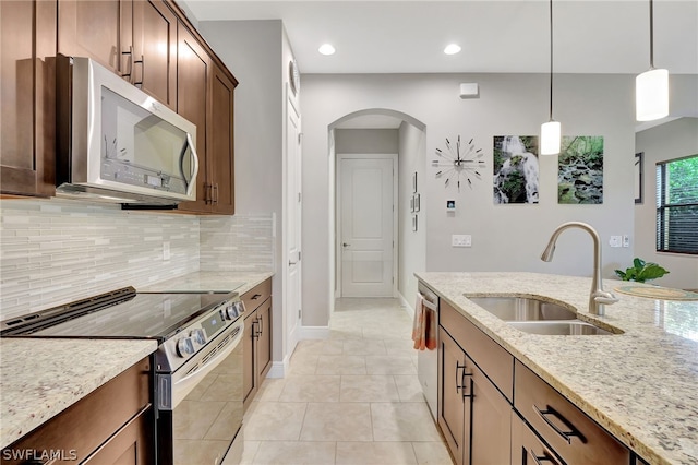 kitchen with arched walkways, decorative light fixtures, light stone countertops, stainless steel appliances, and a sink