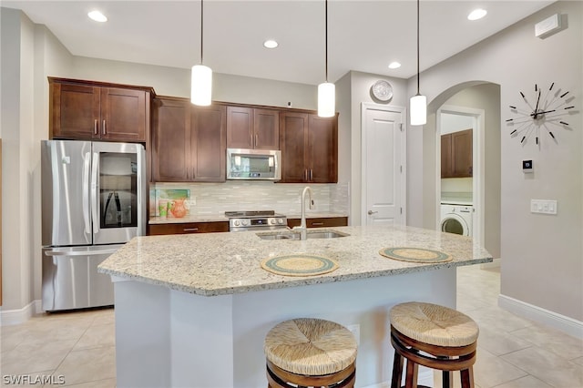 kitchen featuring arched walkways, a sink, appliances with stainless steel finishes, decorative backsplash, and washer / dryer