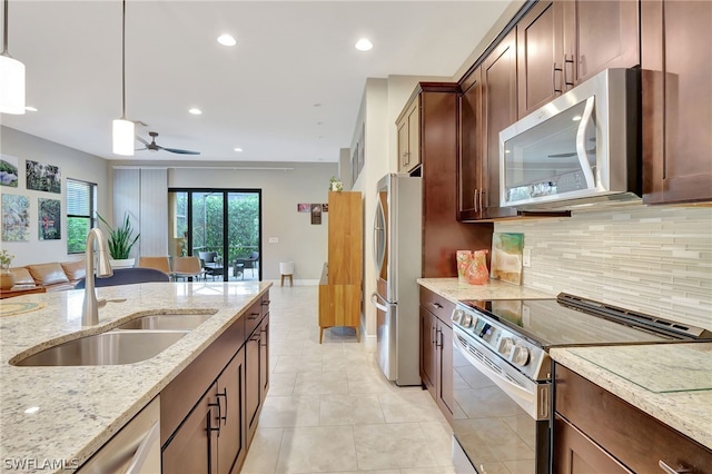 kitchen with light stone counters, decorative light fixtures, backsplash, appliances with stainless steel finishes, and a sink