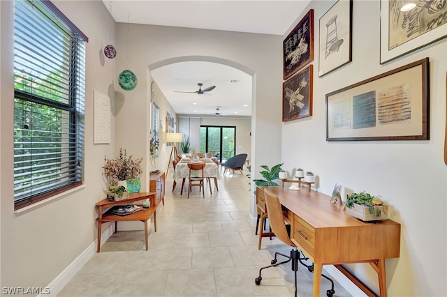 office featuring a ceiling fan, arched walkways, baseboards, and light tile patterned floors