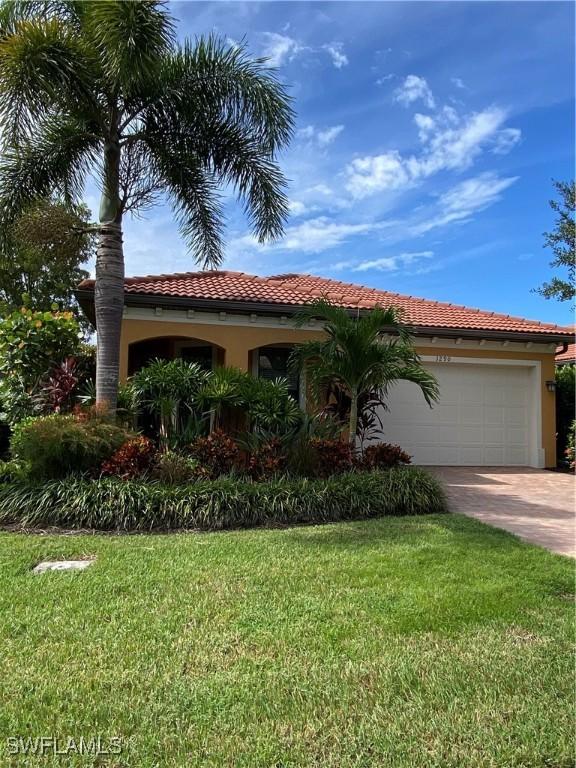 mediterranean / spanish house featuring driveway, stucco siding, a tiled roof, an attached garage, and a front yard