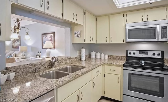 kitchen with a skylight, light stone countertops, cream cabinetry, appliances with stainless steel finishes, and sink