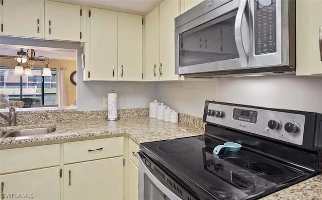 kitchen with sink, light stone counters, appliances with stainless steel finishes, a notable chandelier, and cream cabinets