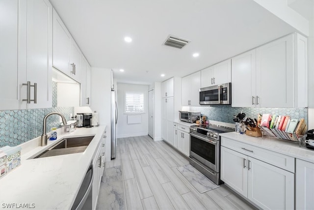 kitchen with visible vents, decorative backsplash, stainless steel appliances, white cabinetry, and a sink