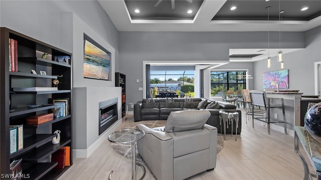 living room with a high ceiling, a tray ceiling, sink, and light wood-type flooring