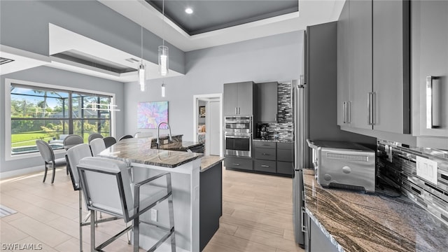 kitchen with decorative light fixtures, dark stone counters, tasteful backsplash, gray cabinetry, and a tray ceiling