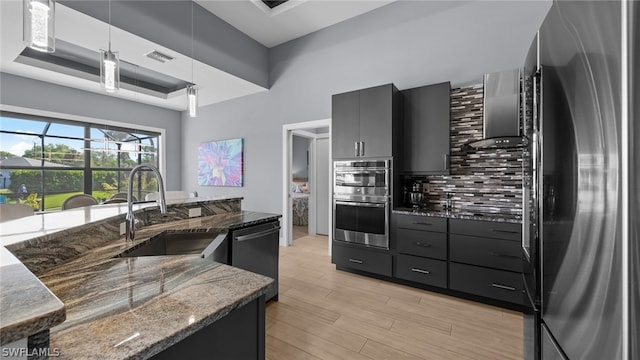 kitchen featuring decorative light fixtures, tasteful backsplash, appliances with stainless steel finishes, a tray ceiling, and dark stone countertops