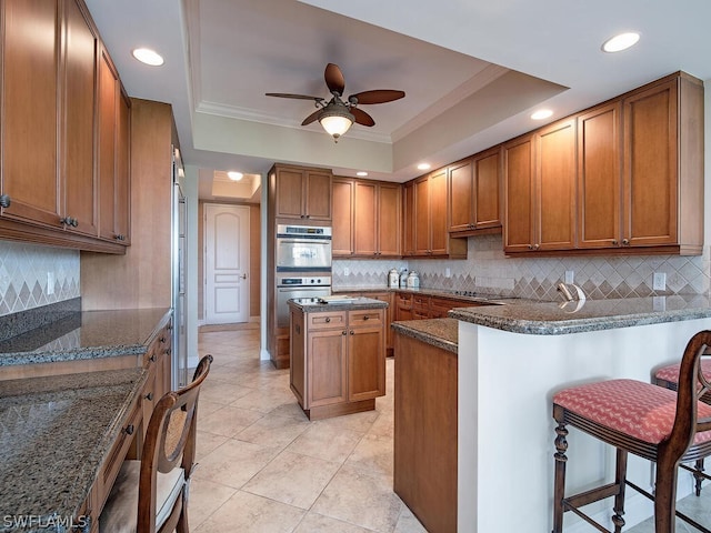 kitchen featuring decorative backsplash, dark stone countertops, a tray ceiling, a kitchen island, and a breakfast bar area