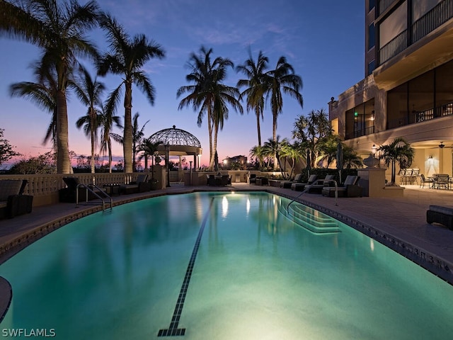 pool at dusk with a gazebo and a patio area