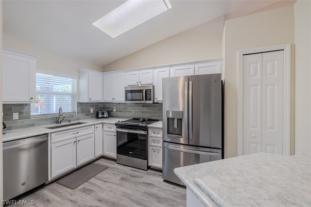 kitchen featuring backsplash, appliances with stainless steel finishes, light wood-type flooring, lofted ceiling with skylight, and white cabinets