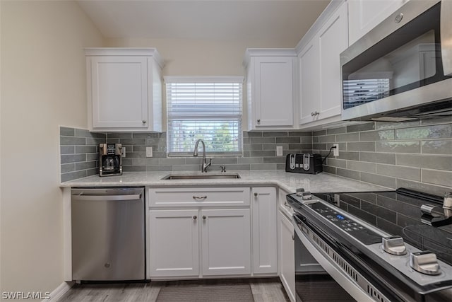 kitchen featuring white cabinetry, sink, light hardwood / wood-style flooring, stainless steel appliances, and tasteful backsplash