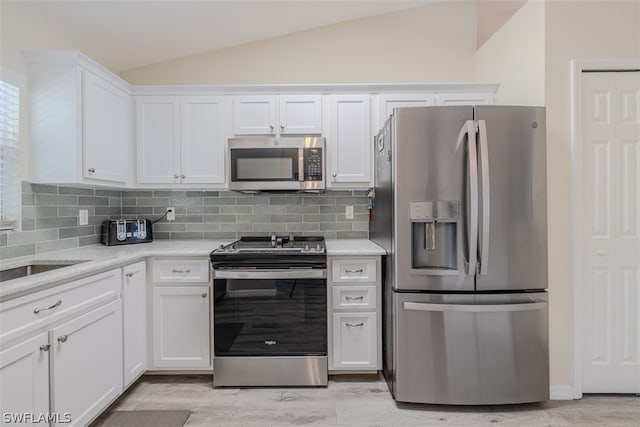 kitchen featuring backsplash, white cabinets, appliances with stainless steel finishes, and lofted ceiling