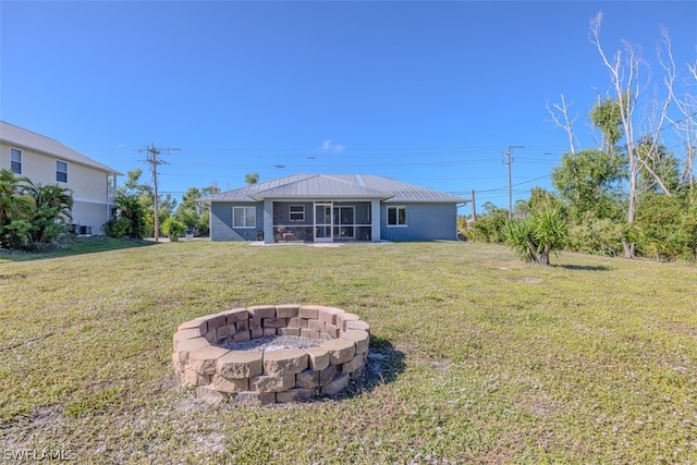 back of house with an outdoor fire pit and a lawn